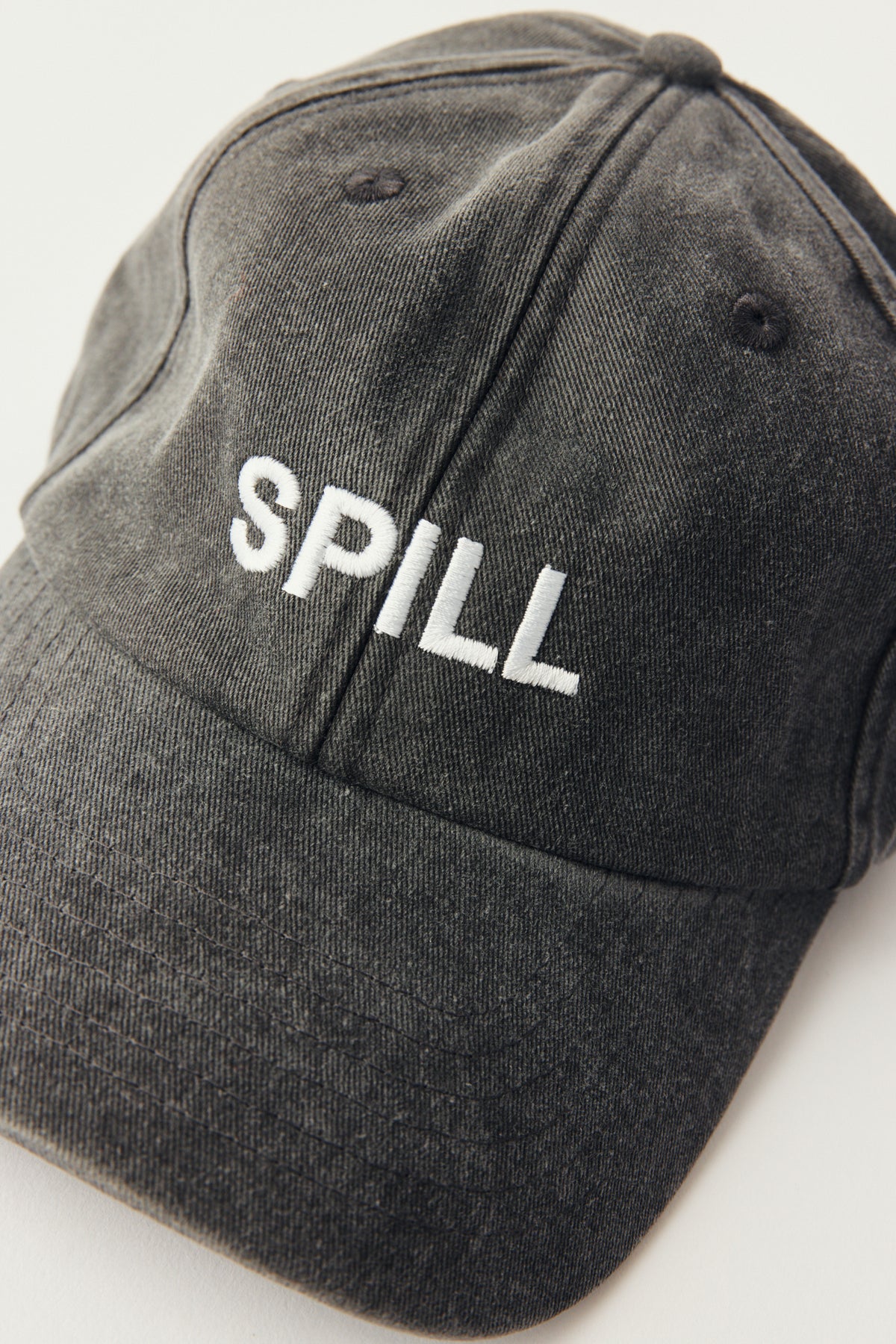 A dark gray washed cotton baseball cap with the word 'SPILL' embroidered in white across the front, shown on a plain light background.
