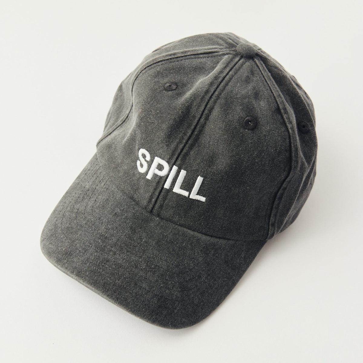 A dark gray washed cotton baseball cap with the word 'SPILL' embroidered in white on the front, photographed on a clean white background.